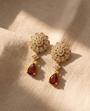 Pair of traditional gold-plated earrings featuring a cz-paved floral stud and a vibrant ruby red pear-shaped teardrop pendant.