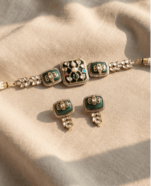 Antique gold choker necklace with dark green enamel and Polki stone details, accompanied by matching square earrings on a neutral fabric.
