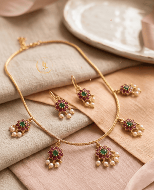 High-angle shot of the Landmark Jewels imitation jewelry set featuring ruby-emerald floral charms and pearls on a neutral fabric background.