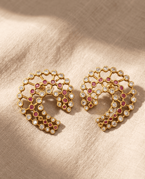 Contemporary gold open C-shaped lattice earrings adorned with small round ruby-pink stones and white stones arranged in concentric rows.