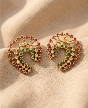 Unique gold-plated crescent horseshoe earrings by Landmark Jewels set with rows of red, green, and clear stones on textured linen fabric.