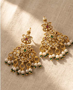 Ornate antique gold chandelier-style earrings featuring clear stones, red and green central gems, and a fringe of white hanging pearls tipped with green beads.