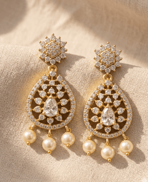 High-shine gold-plated chandelier earrings studded entirely with white cubic zirconia crystals, featuring a central pear-cut stone and hanging pearls.