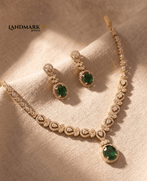 Landmark Jewels emerald green and gold-toned imitation necklace set with matching oval drop earrings on a beige textured fabric background.
