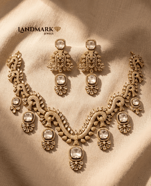 Landmark Jewels gold-plated imitation necklace set with large white cushion-cut stones and matching drop earrings on a textured beige fabric background.