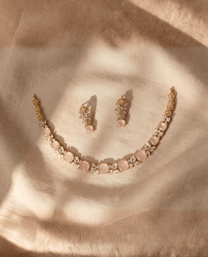 Gold choker necklace with square pastel pink Monalisa stones and clear crystal accents, with matching floral cluster earrings on fabric