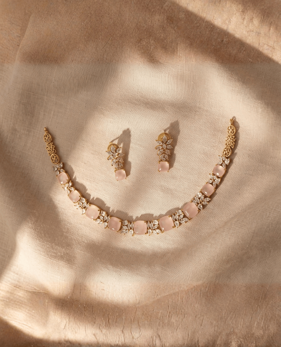 gold-choker-necklace-with-square-pastel-pink-monalisa-stones-and-clear-crystal-accents-with-matching-floral-cluster-earrings-on-fabric