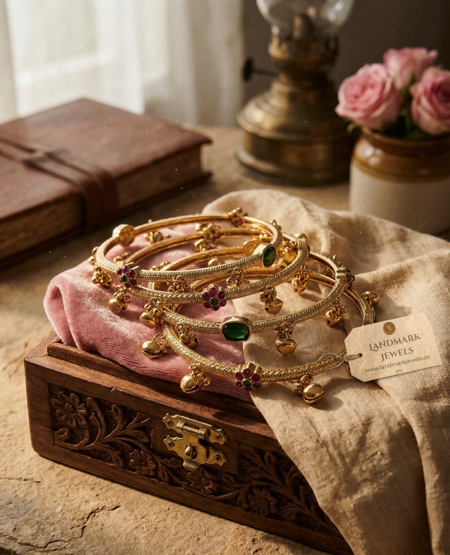 antique-gold-plated-bangles-with-ruby-and-emerald-floral-kemp-stones-and-small-hanging-golden-bells-on-a-peach-fabric-background