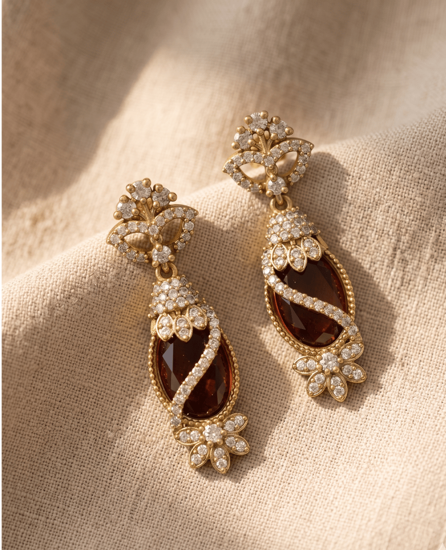 vintage-inspired-long-gold-drop-earrings-showcasing-a-faceted-amber-brown-oval-crystal-wrapped-in-white-stones-on-a-textured-fabric-backdrop