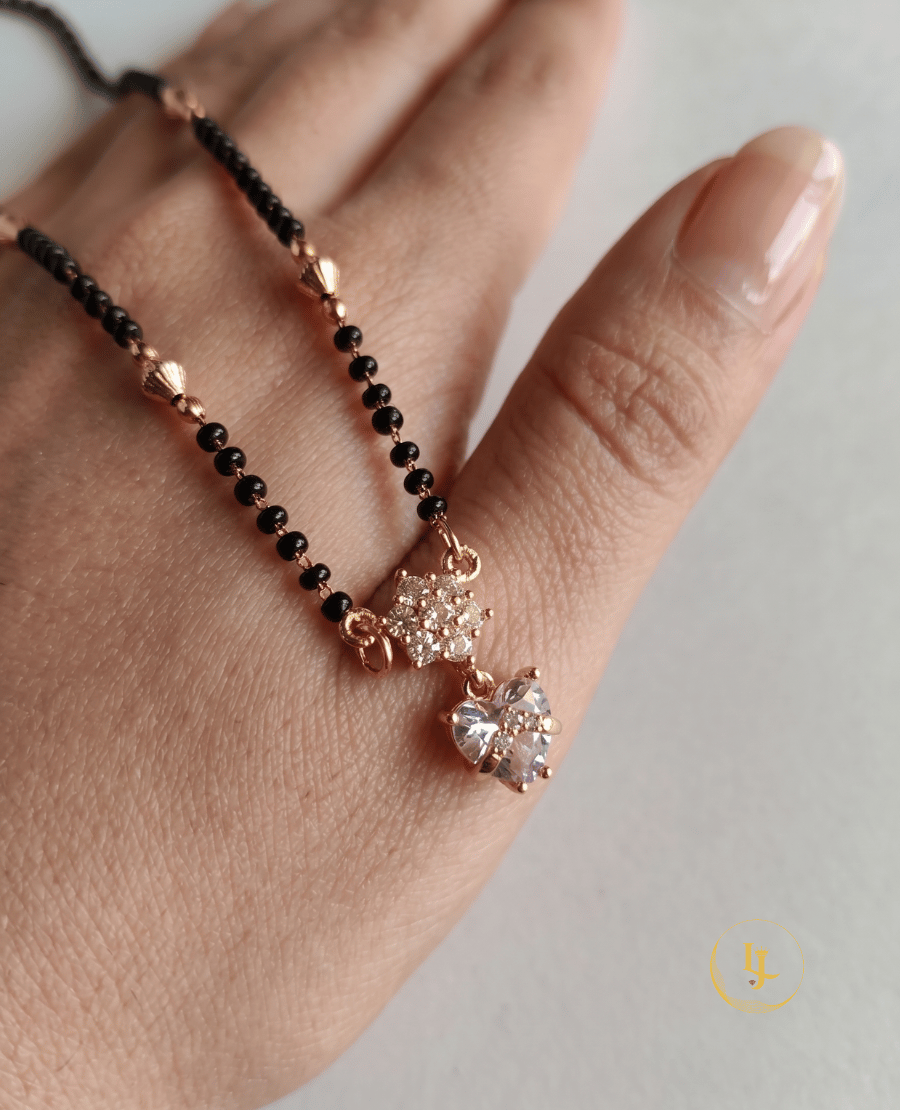 elegant-landmark-jewels-imitation-mangalsutra-featuring-a-single-string-of-black-beads-gold-textured-spacers-and-a-heart-shaped-diamond-look-pendant-on-a-neutral-linen-background