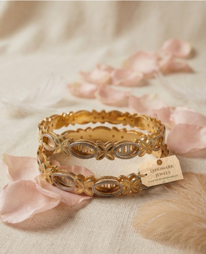Set of two gold and silver dual-tone bangles with butterfly and oval filigree patterns resting on a wooden jewelry box.