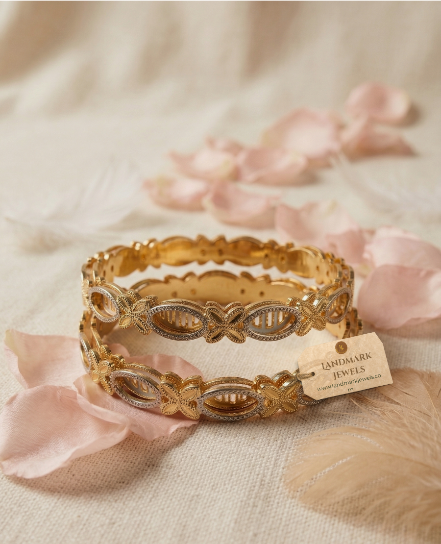 set-of-two-gold-and-silver-dual-tone-bangles-with-butterfly-and-oval-filigree-patterns-resting-on-a-wooden-jewelry-box