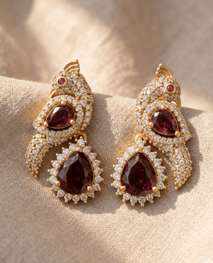 Unique peacock motif earrings from Landmark Jewels crafted with gold plating, crystal pavé detailing, and deep ruby red teardrop stones.