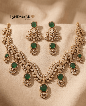 Landmark Jewels gold-plated necklace and earring set featuring emerald green cushion-cut stones and white cubic zirconia accents on a textured beige background.
