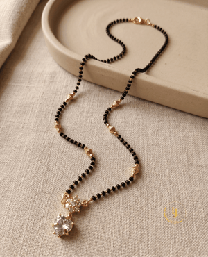 Elegant Landmark Jewels imitation mangalsutra featuring a single string of black beads, gold-textured spacers, and a heart-shaped diamond-look pendant on a neutral linen background.