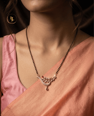 Landmark Jewels imitation mangalsutra with a single strand of black beads and a gold-plated pendant featuring a sparkling CZ-encrusted leaf and vine design on a cream fabric background.