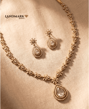 Landmark Jewels American Diamond gold-toned necklace and earring set featuring a large pear-shaped teardrop pendant and floral stone settings on a beige fabric background.