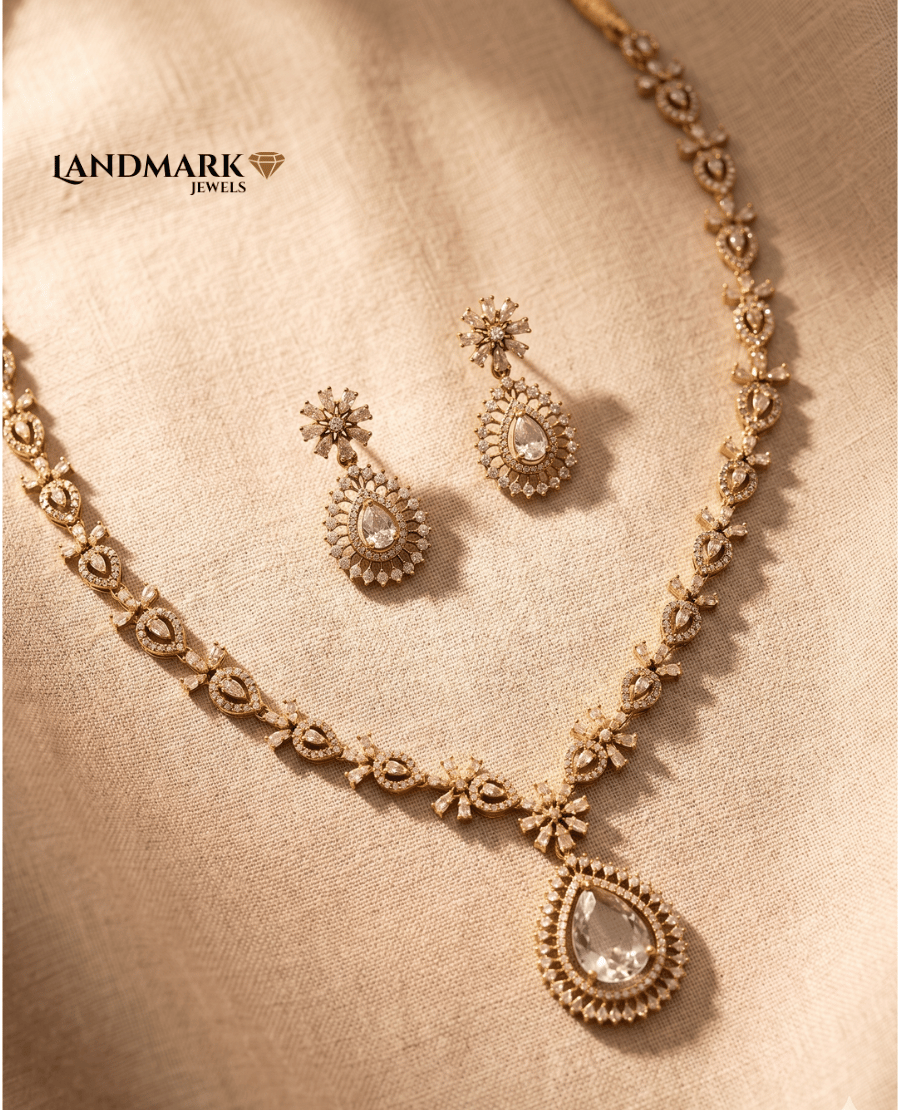 landmark-jewels-american-diamond-gold-toned-necklace-and-earring-set-featuring-a-large-pear-shaped-teardrop-pendant-and-floral-stone-settings-on-a-beige-fabric-background