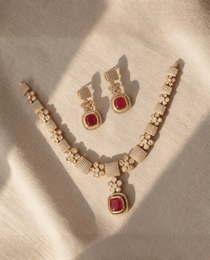 Gold necklace with paved crystal blocks and a vibrant square ruby-red stone pendant, alongside matching cushion-cut ruby earrings