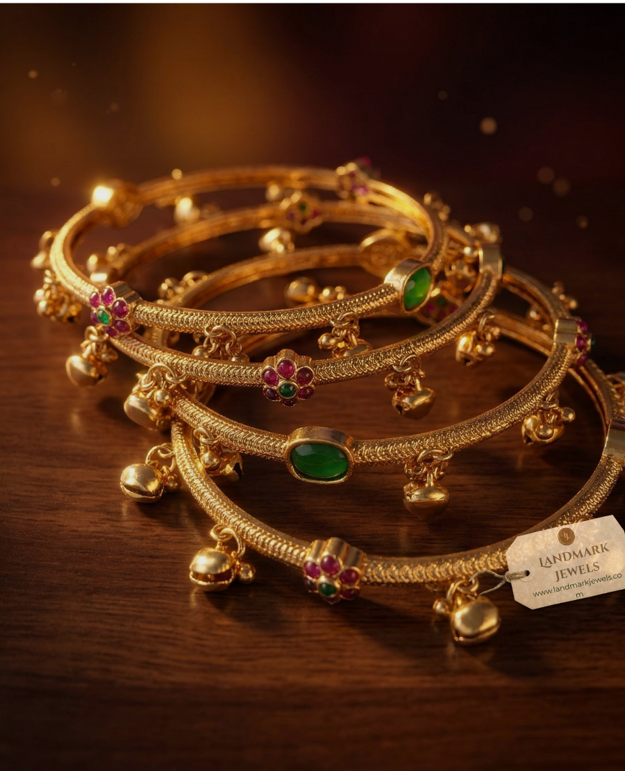antique-gold-plated-bangles-with-ruby-and-emerald-floral-kemp-stones-and-small-hanging-golden-bells-on-a-peach-fabric-background