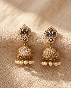 Traditional gold Jhumka earrings by Landmark Jewels featuring a marquise-cut blue sapphire flower stud and a crystal-studded dome with hanging pearl beads.