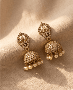 Pair of traditional gold-toned Jhumka earrings covered in clear crystal pave work with an openwork floral top and hanging ivory pearls.