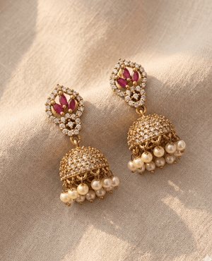 Designer gold-plated jhumkas featuring a diamond-shaped stud with marquise ruby stones and a dense cz-studded dome with pearl fringes.