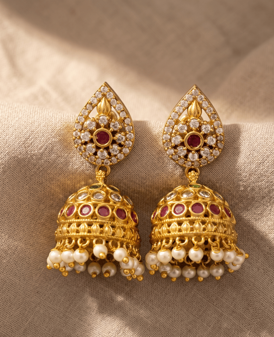 traditional-indian-gold-plated-dome-jhumka-earrings-featuring-ruby-red-round-stones-white-crystal-detailing-and-a-cluster-of-hanging-white-seed-pearls