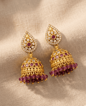 Exquisite gold temple jhumka earrings with emerald green floral accents and clear crystal encrusted domes finished with white hanging pearls.
