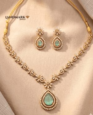 Landmark Jewels gold-toned necklace set featuring mint green pear-shaped stones and white crystal accents with matching drop earrings on a beige fabric background.
