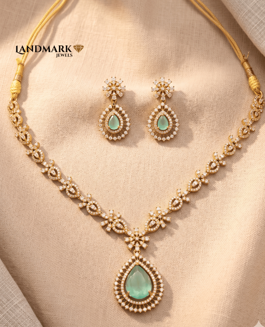 landmark-jewels-gold-toned-necklace-set-featuring-mint-green-pear-shaped-stones-and-white-crystal-accents-with-matching-drop-earrings-on-a-beige-fabric-background