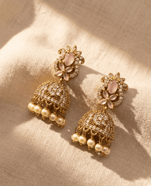 Gold-toned traditional Jhumka earrings with a pastel pink stone floral top, a dome completely covered in white stones, and hanging cream pearls.