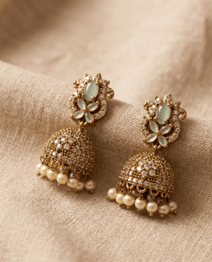 Elegant mint green and gold jhumka earrings featuring a pastel floral stone arrangement and a crystal bell with seed pearl hangings by Landmark Jewels.