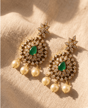 Ornate gold drop earrings by Landmark Jewels featuring a star stud, a crystal filigree disk with a green center stone, and three hanging pearls.