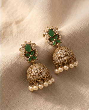 Exquisite gold temple jhumka earrings with emerald green floral accents and clear crystal encrusted domes finished with white hanging pearls.