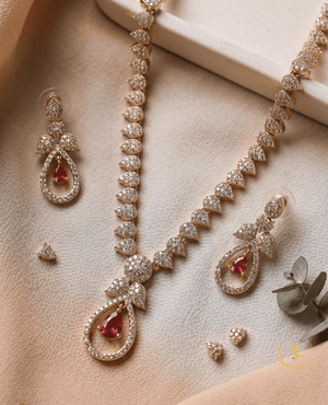 High-resolution flat lay of the rose gold CZ diamond necklace and earring set with ruby accents on a beige fabric background.