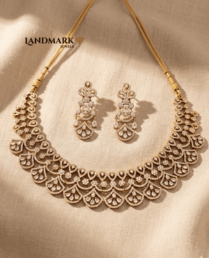 Landmark Jewels gold-plated floral choker necklace and matching drop earrings embellished with white CZ stones on a beige fabric background.