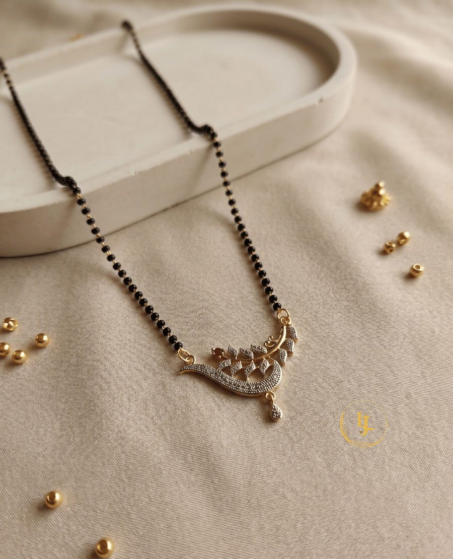 landmark-jewels-imitation-mangalsutra-with-a-single-strand-of-black-beads-and-a-gold-plated-pendant-featuring-a-sparkling-cz-encrusted-leaf-and-vine-design-on-a-cream-fabric-background