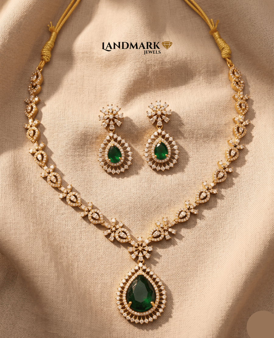 landmark-jewels-gold-plated-necklace-set-featuring-a-large-emerald-green-teardrop-pendant-and-matching-floral-drop-earrings-on-a-beige-fabric-background