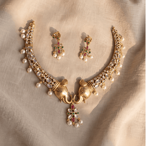 Unique antique gold choker with sculpted elephant head designs, encrusted with Polki stones and hanging pearls, alongside matching traditional earrings.