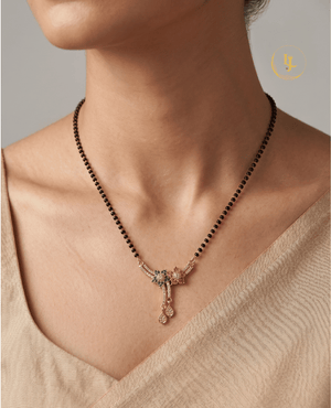 Landmark Jewels gold-plated short mangalsutra with floral American Diamond pendant, green and pink stones, and traditional black beads on a beige fabric background.