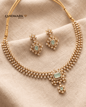 Landmark Jewels gold-plated necklace set featuring a mint green rectangular emerald-cut stone and sparkling American Diamond floral motifs on a textured fabric background.