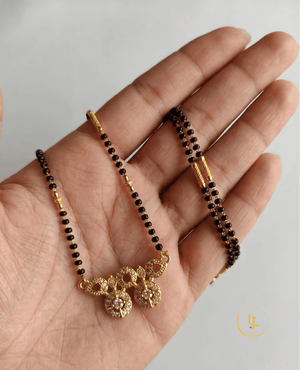 Landmark Jewels modern mangalsutra featuring a single strand of black beads with gold pipe spacers and a geometric gold pendant made of CZ-studded circles on a textured fabric.