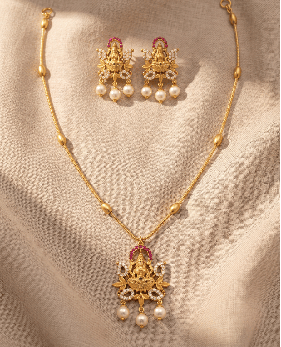 matte-gold-temple-necklace-with-a-goddess-lakshmi-pendant-framed-by-red-stones-and-pearls-alongside-matching-lakshmi-stud-earrings