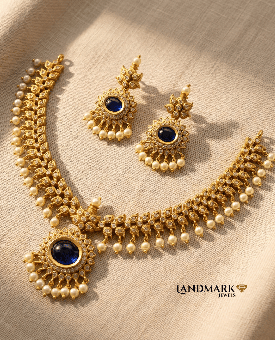 landmark-jewels-antique-gold-necklace-and-earring-set-featuring-central-royal-blue-kemp-stones-white-crystals-and-dangling-pearls-on-a-beige-fabric-background