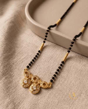 Landmark Jewels modern mangalsutra featuring a single strand of black beads with gold pipe spacers and a geometric gold pendant made of CZ-studded circles on a textured fabric.