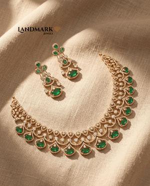Landmark Jewels imitation jewelry set featuring a gold-plated choker and matching drop earrings studded with emerald green stones and American Diamonds on a beige fabric background.