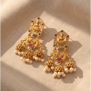 Traditional antique gold temple jhumka earrings featuring Goddess Lakshmi, ruby stones, and hanging pearls on a neutral fabric background.