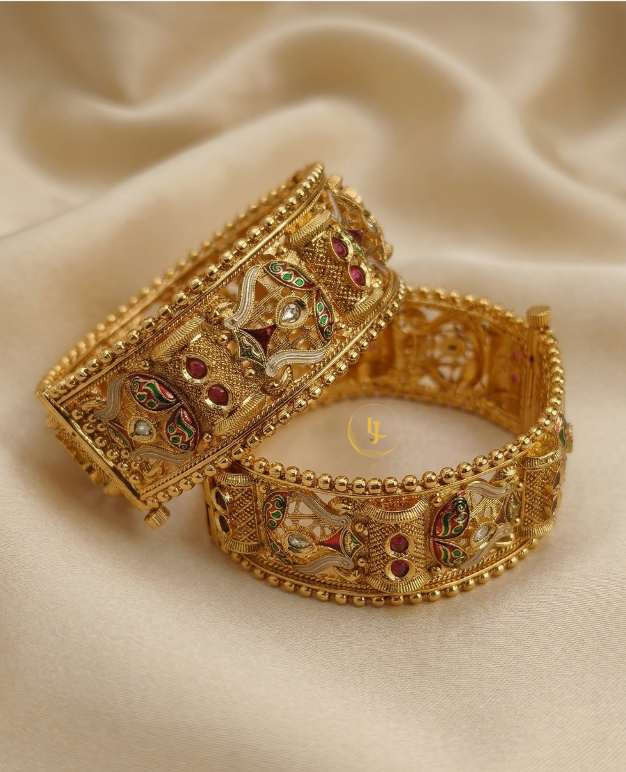 pair-of-antique-gold-plated-meenakari-kada-bangles-with-green-and-red-enamel-work-and-ruby-stone-accents-on-a-beige-silk-background