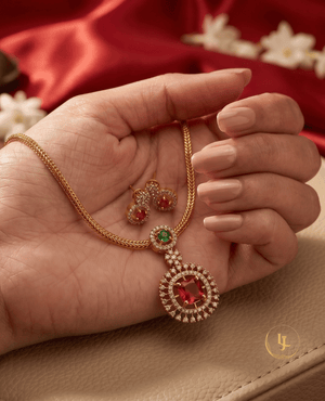 Handheld view showing the scale and detail of the gold-plated emerald green bird pendant and earrings by Landmark Jewels.